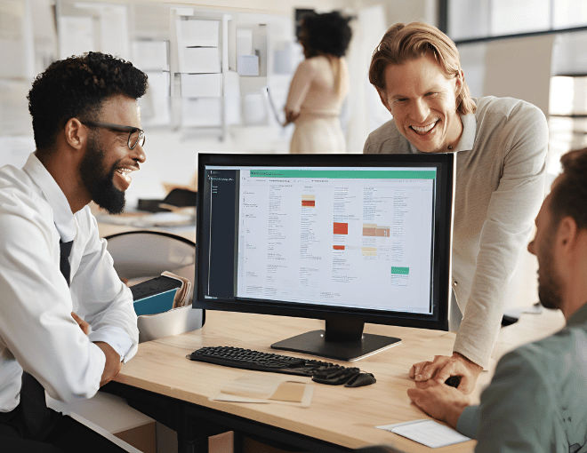 People in an office setting using a computer, reviewing file conversion software options displayed on the monitor, discussing features and compatibility.